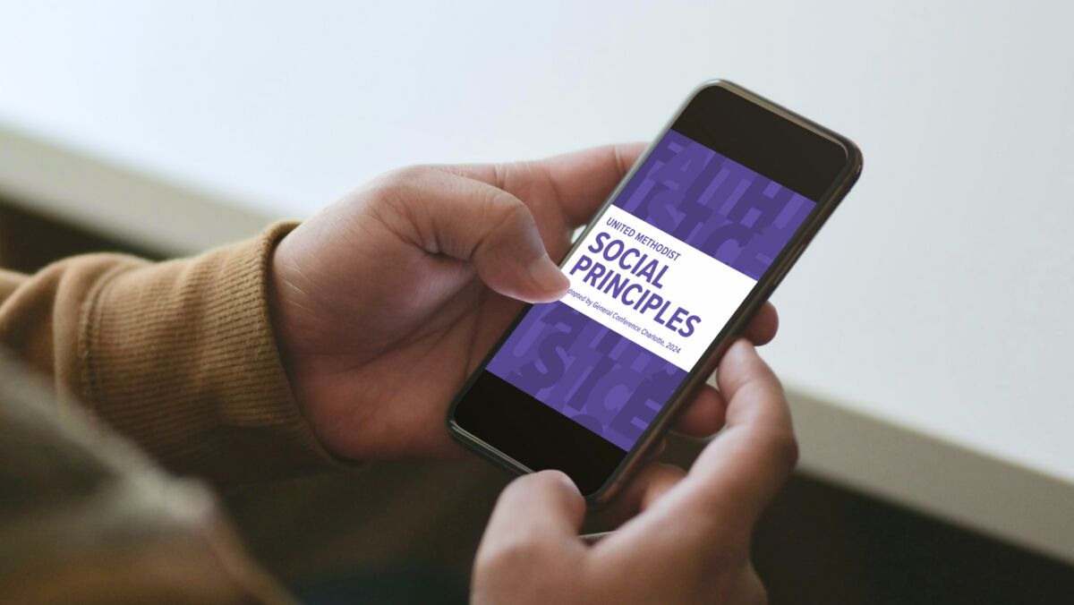 A person holding a phone. On the phone is the cover of the Social Principles 2024.